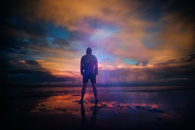 Man standing looking up into a beautiful sky scape representing mans personal journey to find if God cares for us