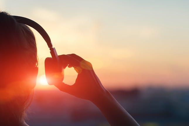 silhouette at sunset of person with headphones on, pulling one earpiece away, representing the pursuit of hearing God.