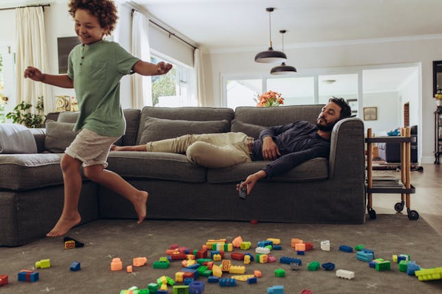 Kid playing with legos while dad lays on the couch.