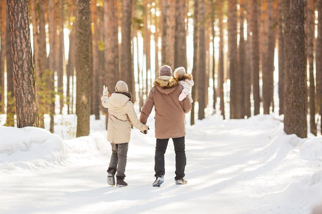 Couple holding hands and carrying small child in snowy forest,